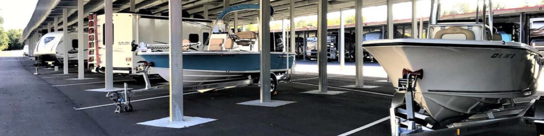 Covered carport storage with center-console boats on trailers and RVs parked in rows at a boat and RV storage facility.
