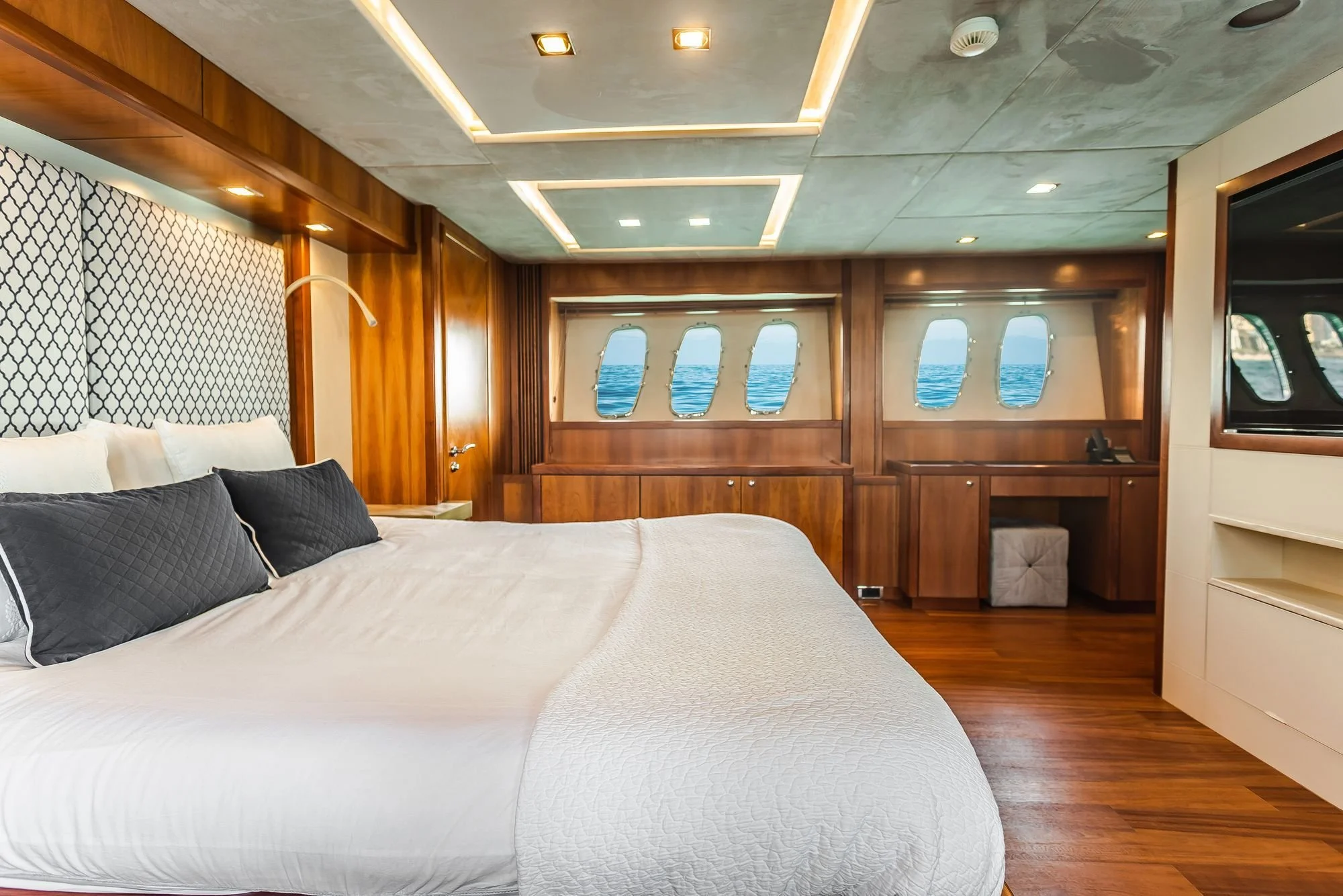 Luxury yacht master stateroom with a made bed, polished teak cabinetry, and portholes overlooking open water.