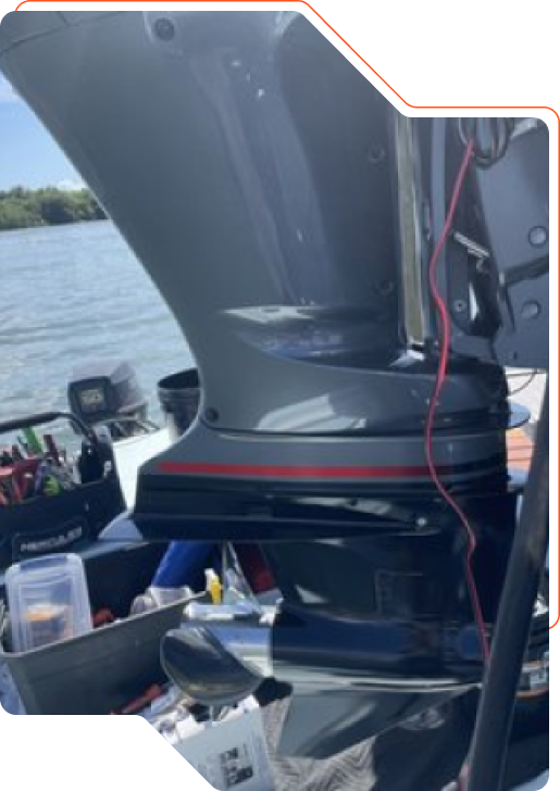 Outboard motor mounted on a boat transom, with a toolbox and fishfinder on deck above open water.