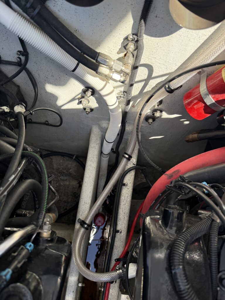 Engine compartment of a boat showing hoses, wiring, and a mounted fire extinguisher, with no business name or town identifiable.