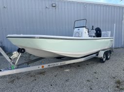 White center-console fishing boat on a trailer parked outside a metal building.