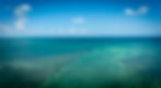 Turquoise shallow reef water stretching toward the horizon under a partly cloudy blue sky.