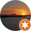 Sunset over calm coastal water with distant shoreline structures, business and town not identified.