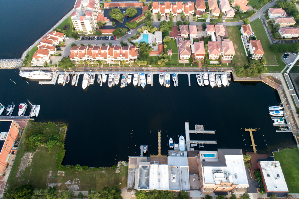 Aerial view of yachts and boats docked at a residential waterfront marina lined with terracotta-roofed condominiums.
