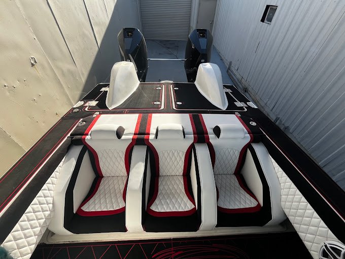 Stern view of a performance boat with white diamond-quilted seating trimmed in red and black, and twin outboard motors, shown in a storage area.
