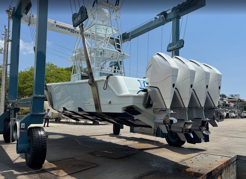Center console sportfishing boat with four outboard engines suspended in a Marine Travelift at a boatyard.