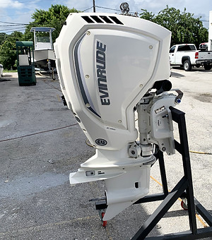 White Evinrude outboard motor on a black stand in an outdoor boat yard with a boat and pickup truck in the background.