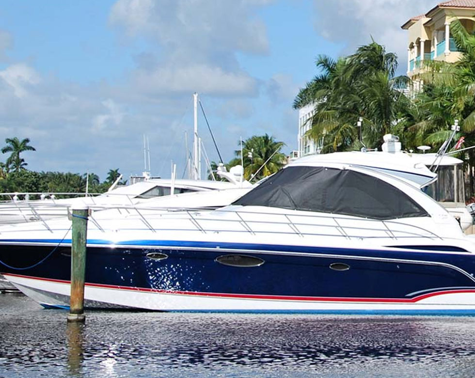 Blue and white motor yacht moored at a marina dock with palm trees and waterfront buildings behind it.