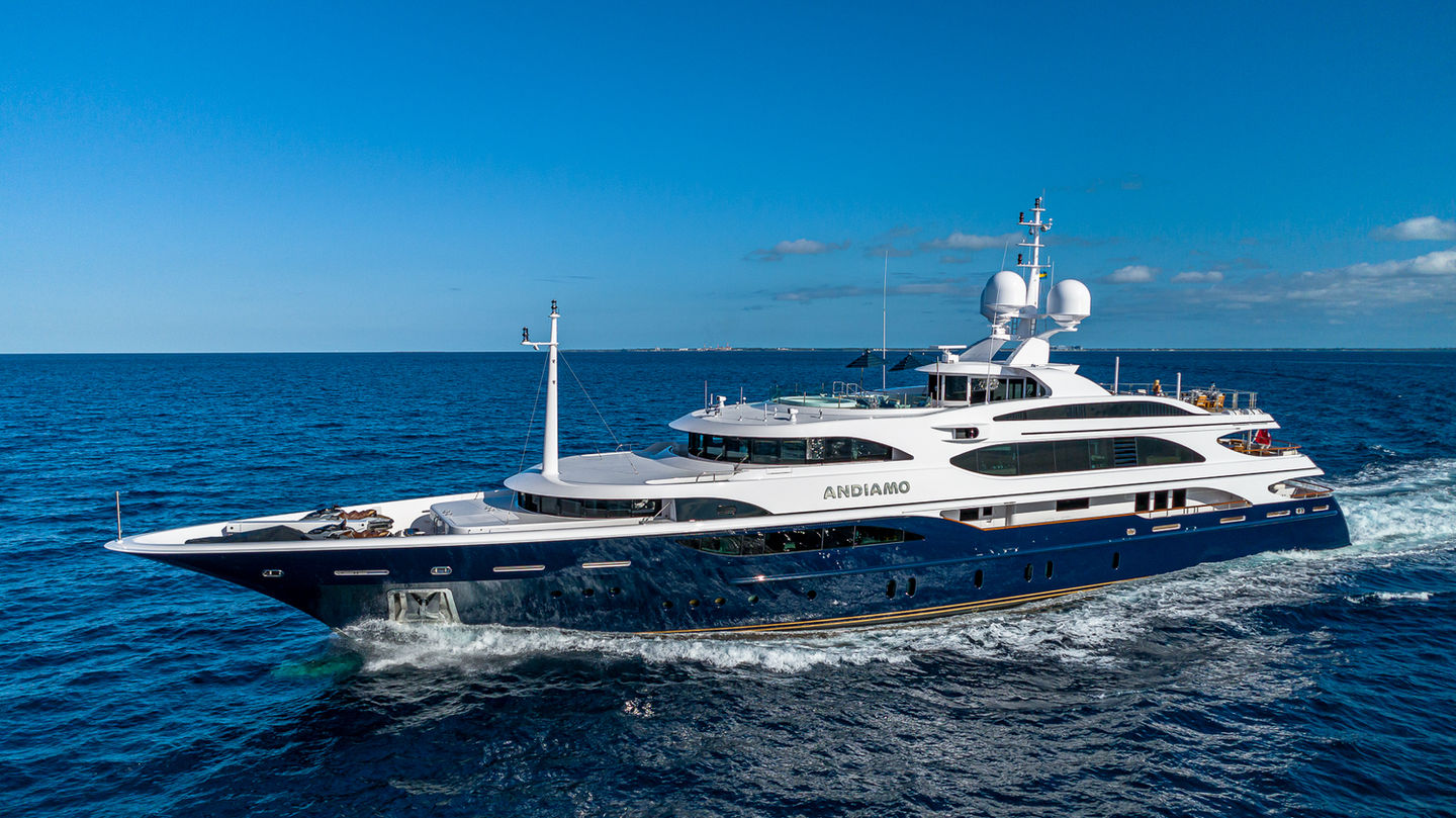 Motor yacht ANDIAMO with a navy hull and white superstructure cruising across open blue water under a clear sky.