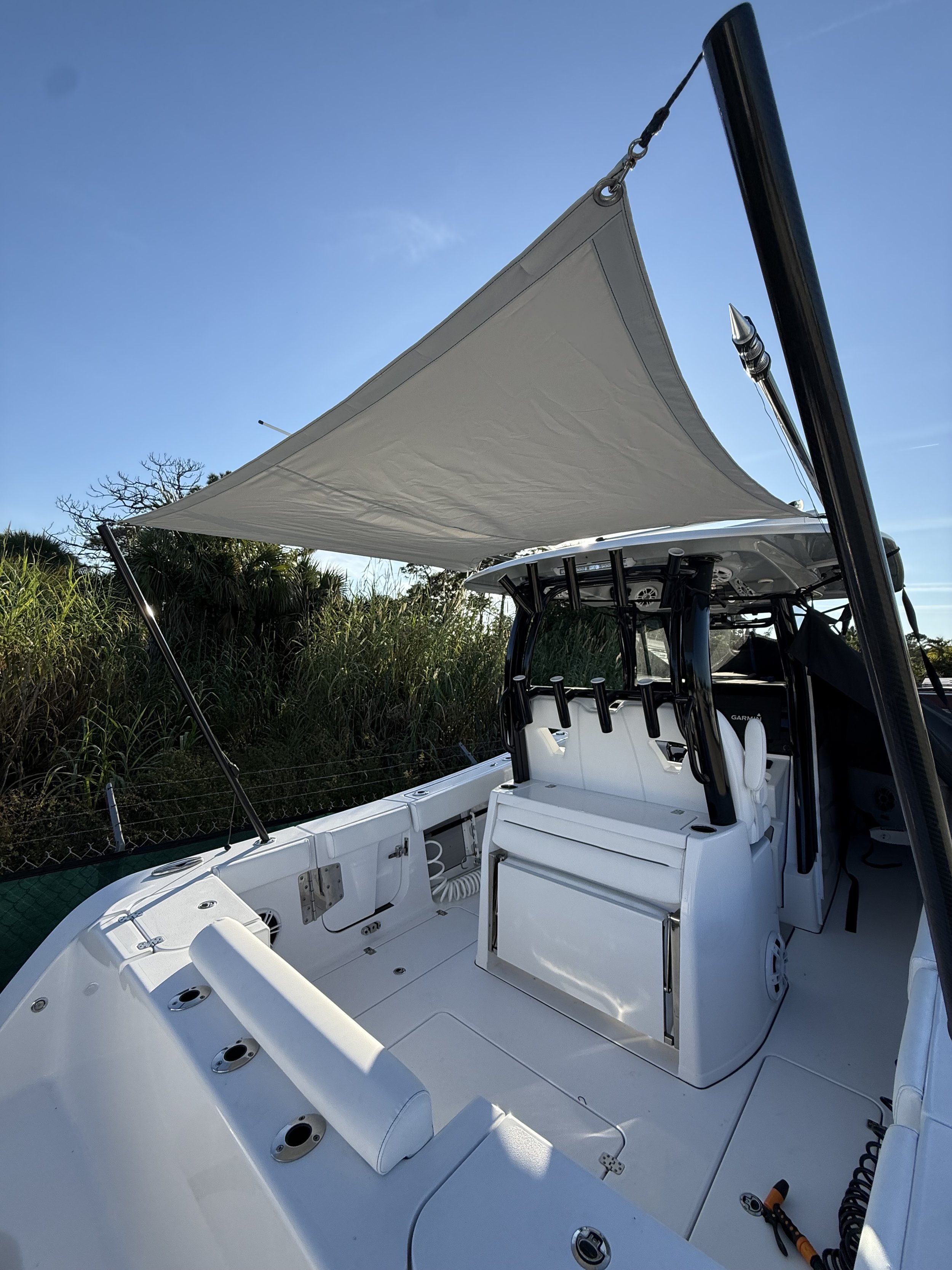 Center console fishing boat with a triangular sun shade over the leaning post and cockpit, showing rod holders and a Garmin helm display.