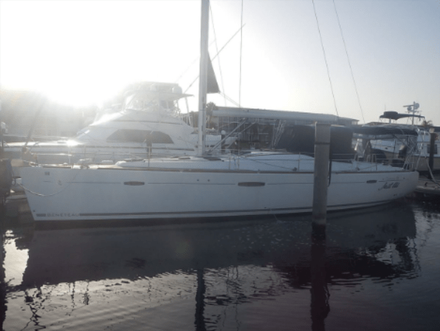 White sailboat moored at a marina dock with a motor yacht in the background, shot in bright morning light.