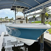 Light blue center-console boat lifted on a dock lift beneath a canopy along a residential canal.
