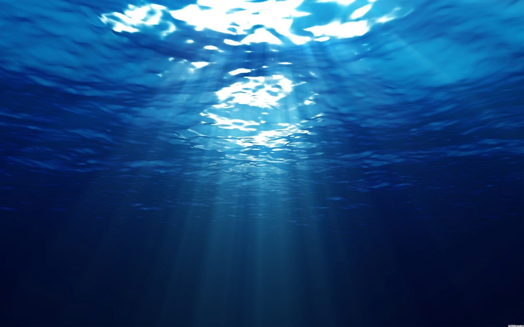 Sunlight rays filtering through rippling blue ocean water, viewed from below the surface.
