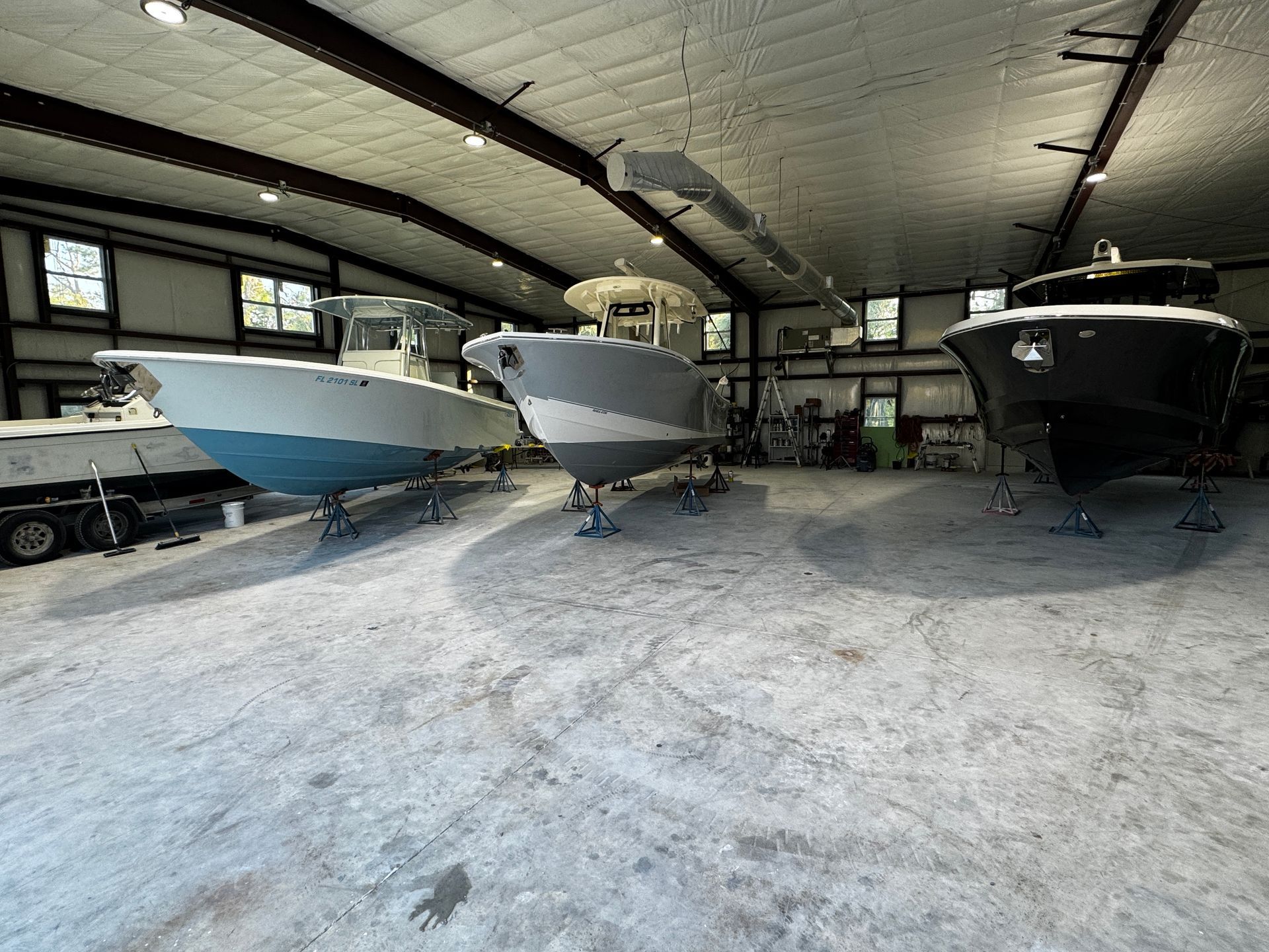 Three center-console boats raised on jack stands inside a metal-frame boat shop, one showing a Florida registration number FL 2101 SL.