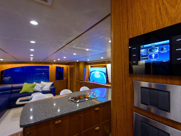 Yacht salon interior showing a granite galley counter, blue leather seating, and a Garmin touchscreen control panel for lighting and cameras.