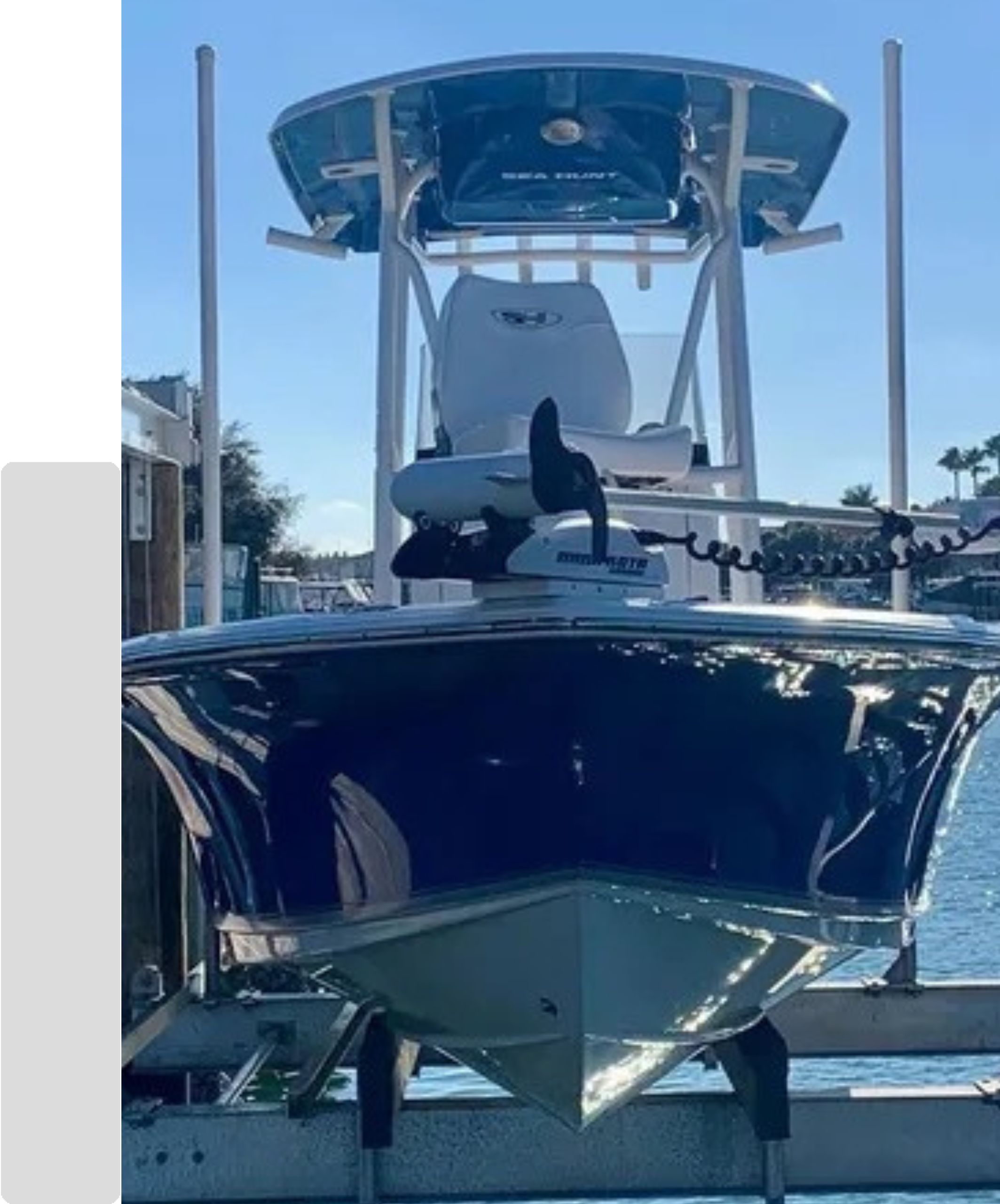Dark blue center console boat with a white T-top and bow-mounted trolling motor docked at a marina.