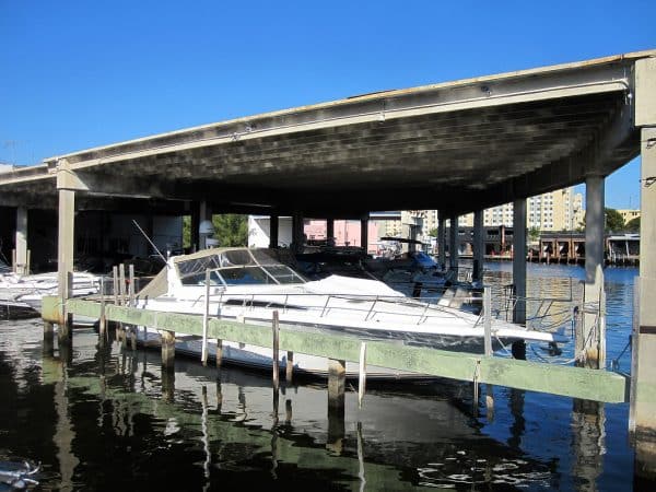 White sport cruiser boat under a covered dock structure on a canal waterfront, with other boats moored alongside.