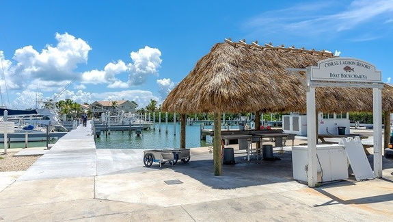 Thatched-roof pavilion and dock walkway at Coral Lagoon Resort Boat House Marina, with moored boats along the water.