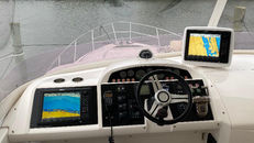 Boat helm station with a steering wheel and two marine chartplotter displays showing sonar and navigation charts.