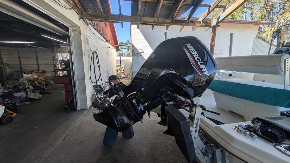 Mercury outboard motor being serviced on a center-console boat in a covered repair shop bay.