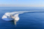 White motorboat leaving a long wake across calm blue open water.