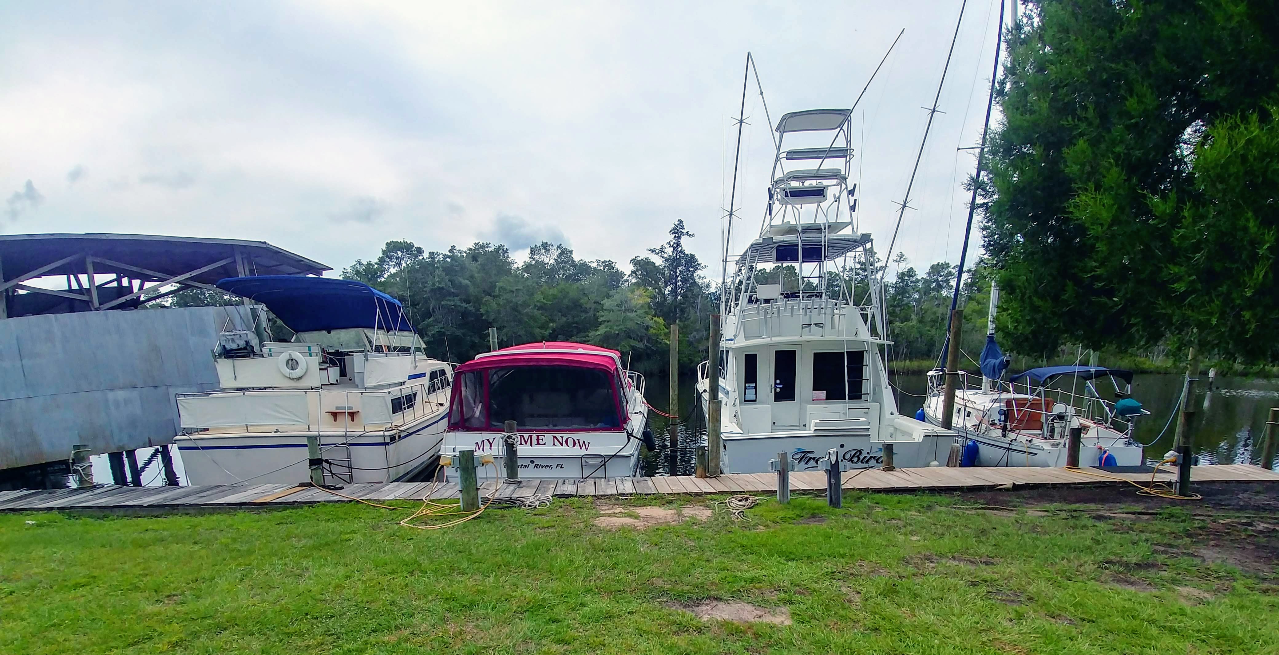 Moored sportfishing and cruising boats at a wooden dock with a covered boat shelter, Crystal River, FL.