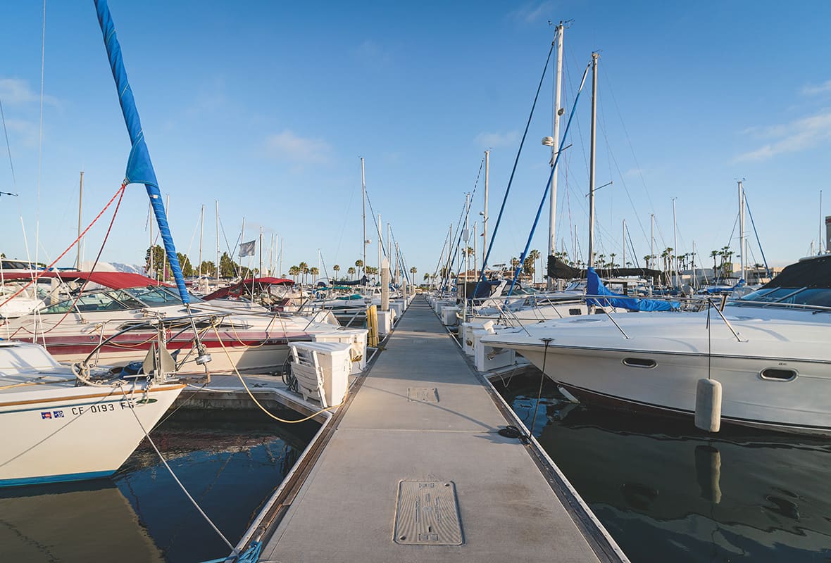 Floating dock lined with sailboats and motor yachts at a marina harbor.