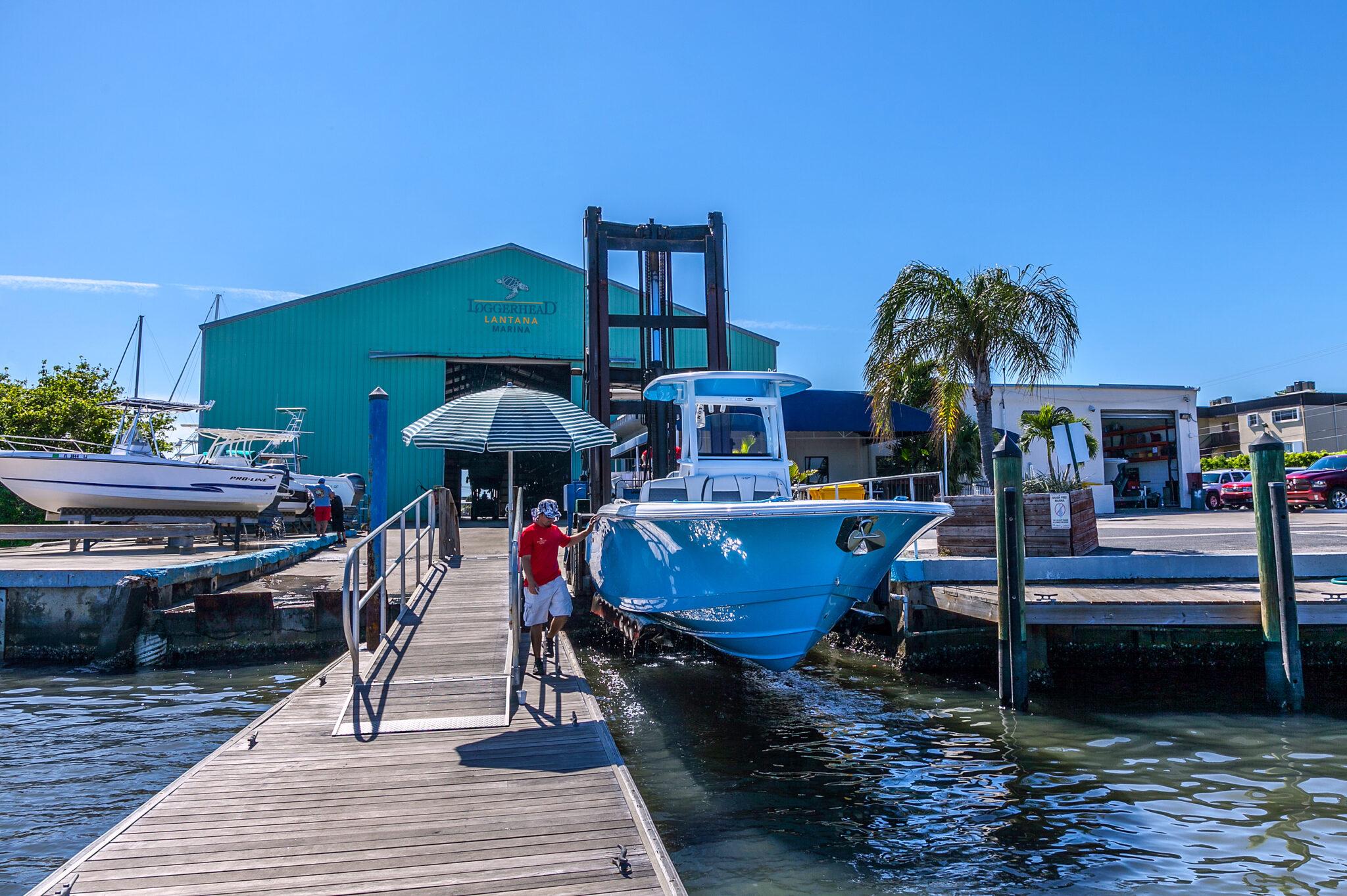 Blue center-console boat being lifted by a travel lift at Loggerhead Marina, Lantana.