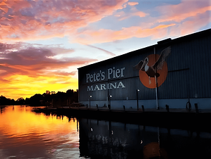 Sunset over the water at Pete's Pier Marina, with the marina building and its signage along the waterfront.