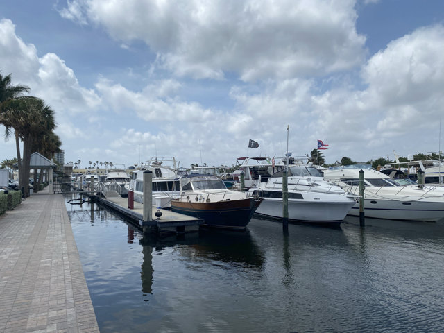 Motor yachts and a classic wooden launch moored at a marina dock with a brick walkway along the water.