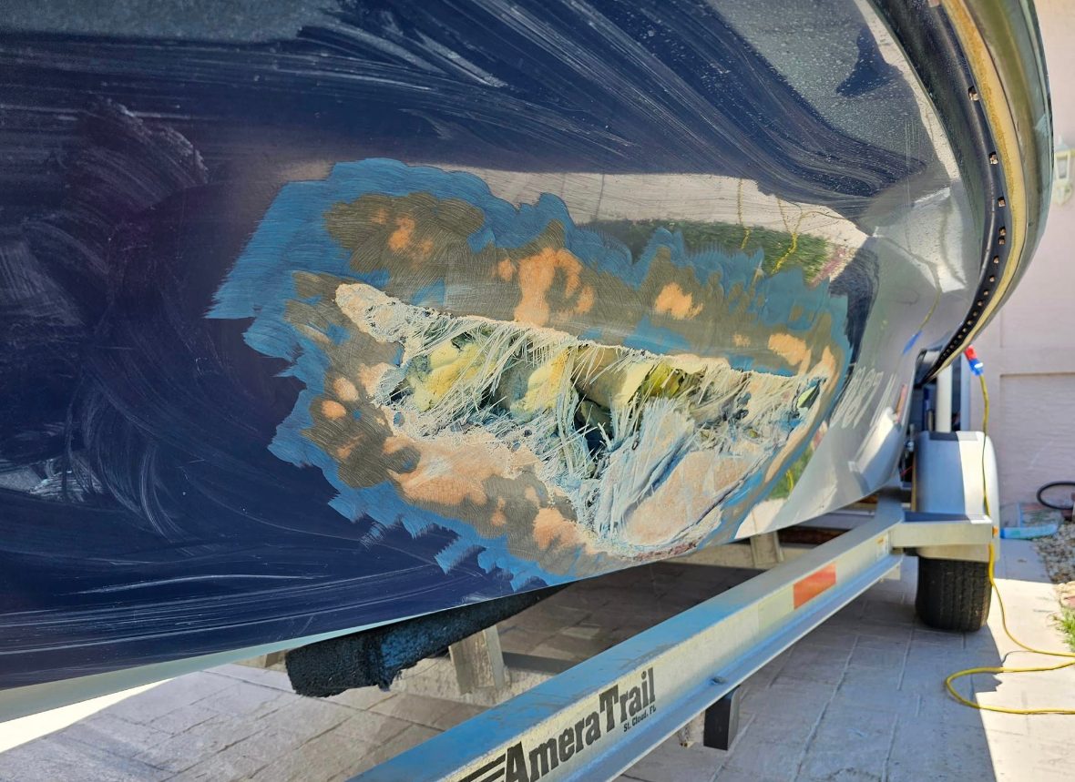 Boat hull with a large section of damaged gelcoat ground down to exposed fiberglass laminate on an AmeraTrail trailer.