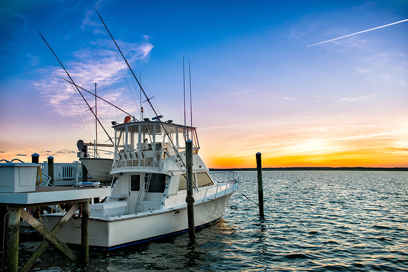Sportfishing boat with tall rigging and rod holders moored at a wooden dock during sunset.
