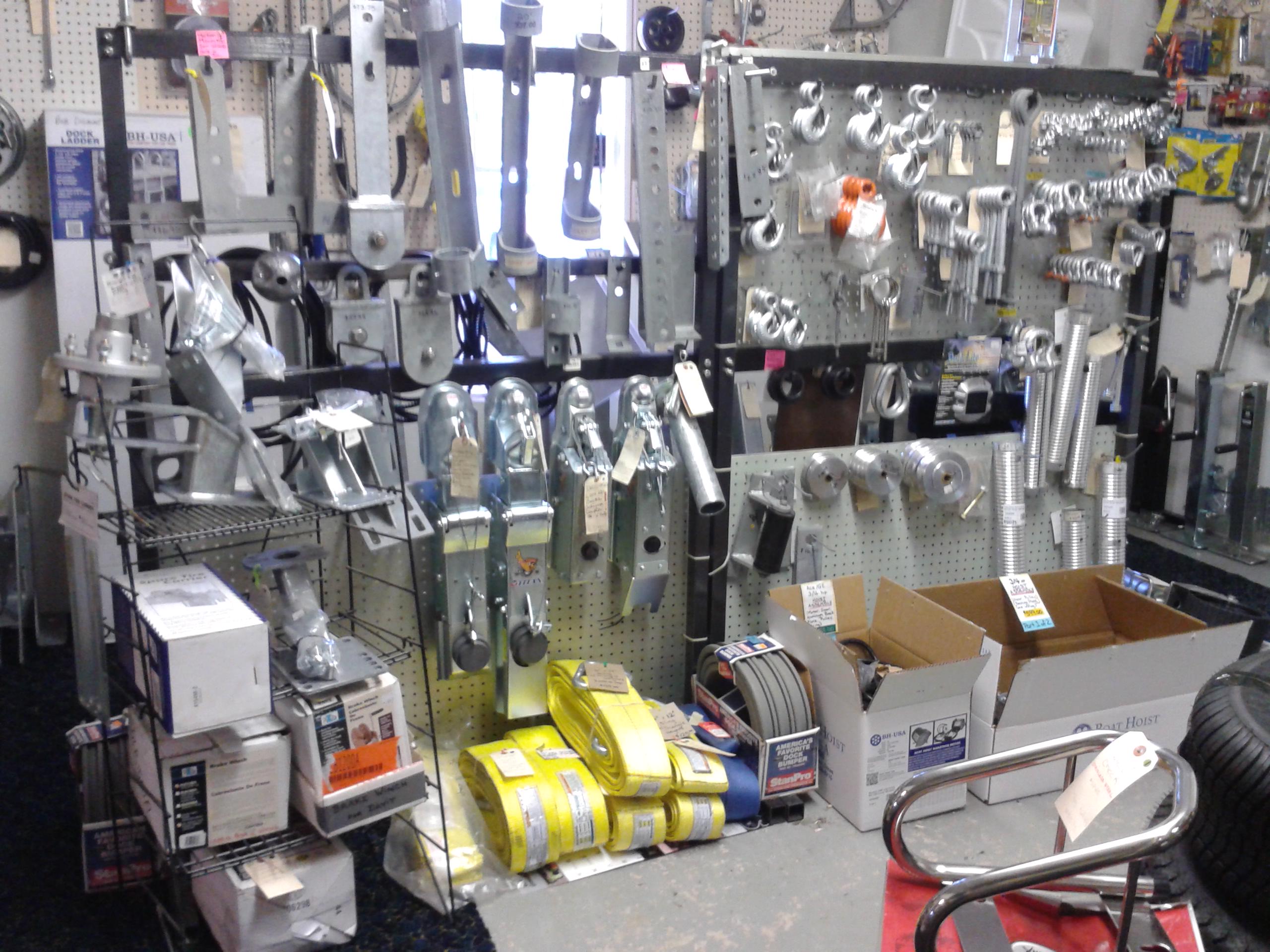 Marine hardware display of trailer couplers, dock ladder, yellow winch straps, and BH-USA boat hoist parts inside a marine supply store, town unknown.