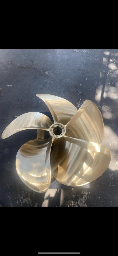 Five-blade bronze boat propeller resting on a concrete floor, likely after removal or refurbishment.
