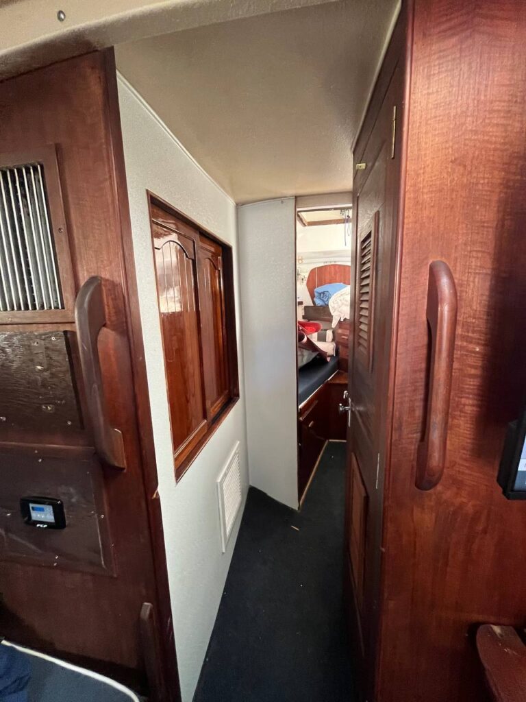 Interior passageway of a sailing yacht with varnished mahogany cabinets and a forward berth visible at the end of the corridor.