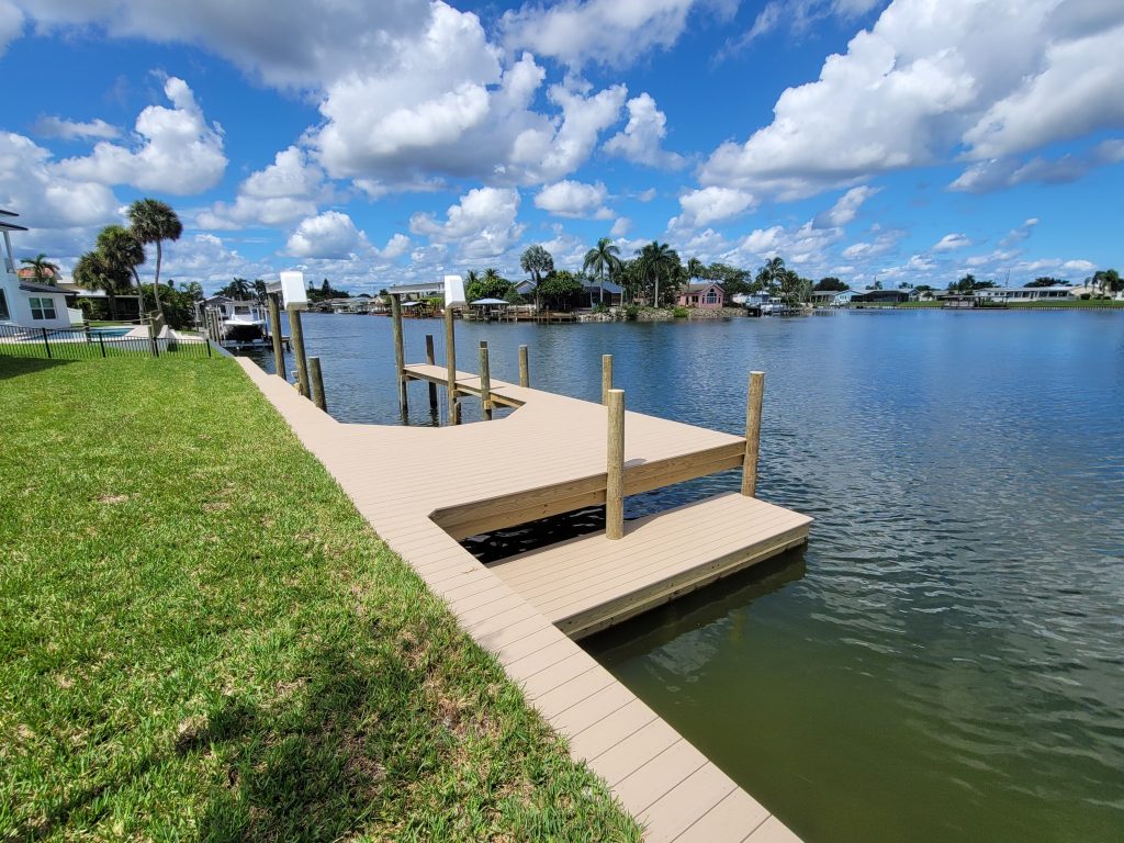 Newly built composite dock with boat lift pilings on a residential canal waterfront with palm trees and homes across the water.