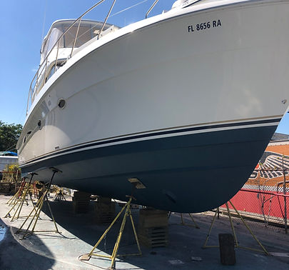 Motor yacht with white hull and dark blue bottom paint on jack stands in a Florida boatyard.