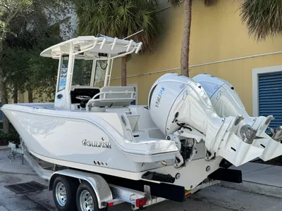 White Sailfish-style center-console boat with twin Yamaha outboard motors sitting on a dual-axle trailer in front of a yellow building.