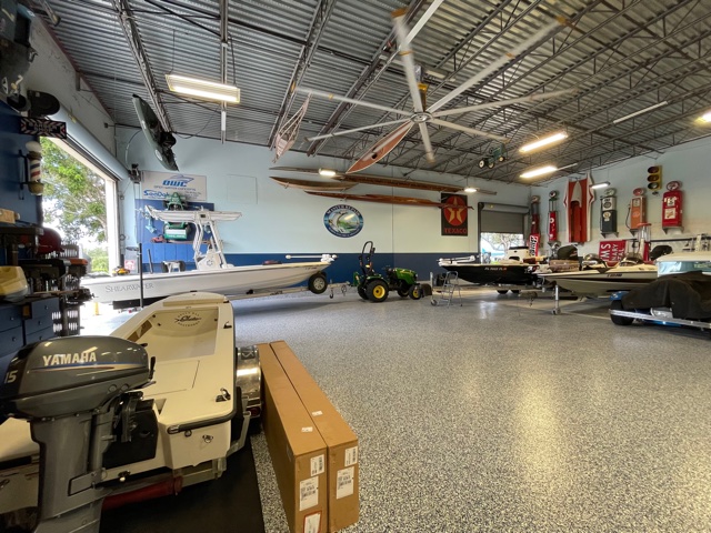 Interior of a boat showroom with center console boats and a Yamaha outboard motor on display, with a green tractor and wall-mounted boat memorabilia.