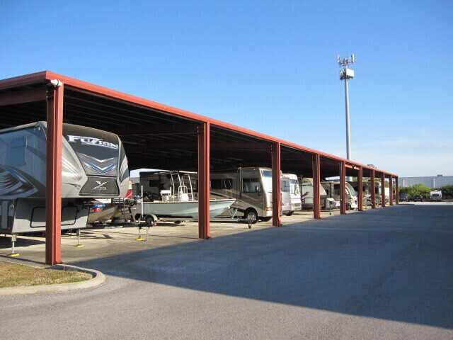 Covered outdoor storage carports holding RVs, a travel trailer, and a small boat on a trailer, with no business name or town visible.