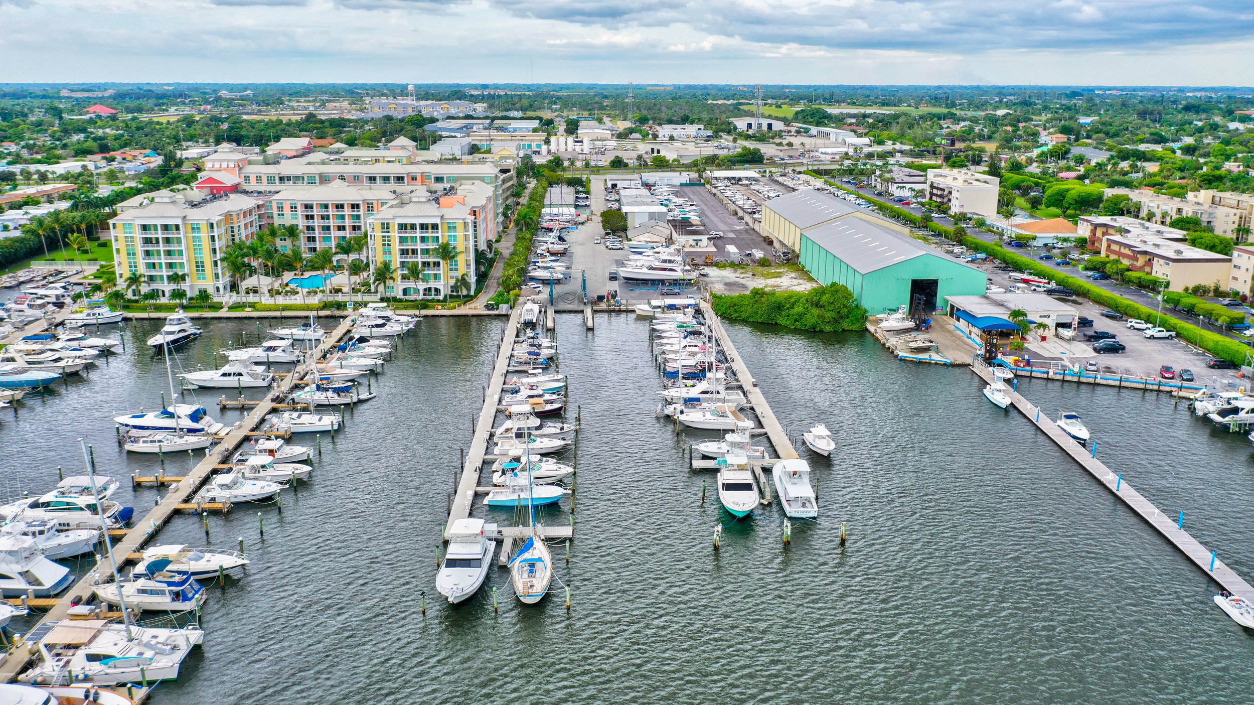 Aerial view of a marina with docked boats, a boat storage yard, and a boat repair shed on the waterfront.