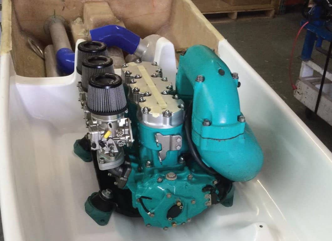 Teal marine engine with individual pod air filters sitting in a white fiberglass hull in a workshop.