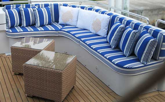 Blue and white striped curved deck seating with wicker side tables on a teak-decked yacht.