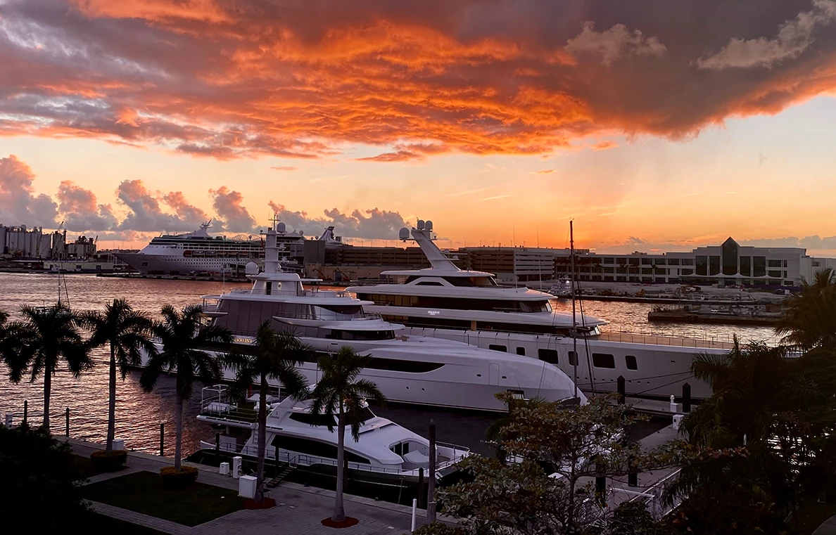 Superyachts moored at a waterfront marina with a cruise ship in the background at sunset, Fort Lauderdale.