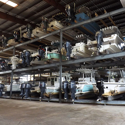 Outboard motorboats stored on multi-tier steel racks inside an indoor boat storage facility, business and town not identified.
