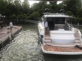 Motor yacht moored at a wooden dock on a tree-lined waterway.
