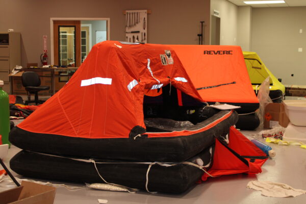 Revere inflatable life rafts with orange canopies being serviced in a workshop.