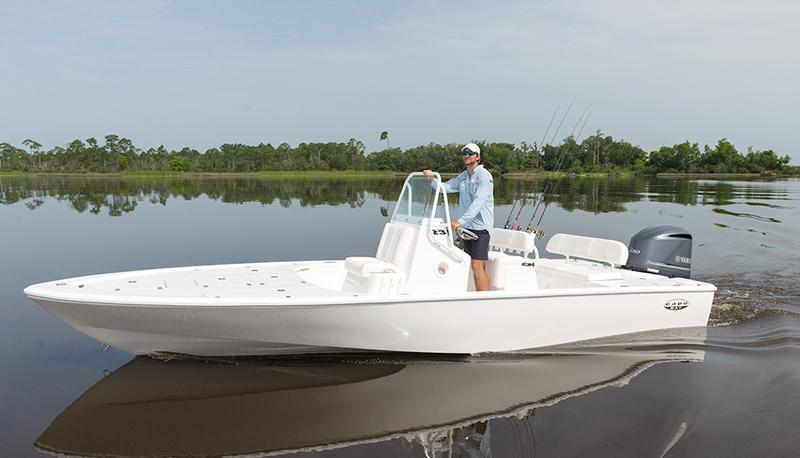 White center-console bay boat with a Yamaha outboard cruising on calm water past a tree-lined shoreline.