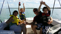 Four people relaxing and cheering on the deck of a motorboat on open water.