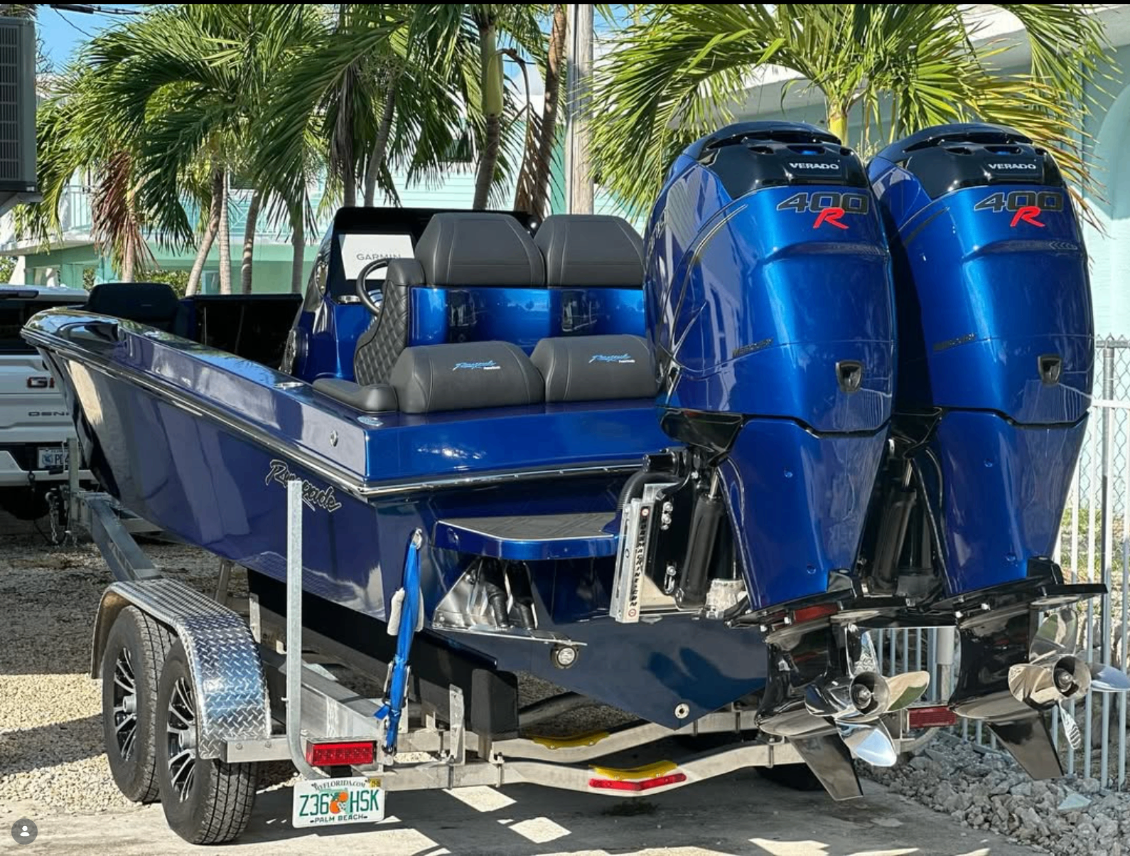 Blue Renegade center console boat with twin Verado 400R outboard motors on a trailer in a gravel lot lined with palm trees, Palm Beach, Florida.